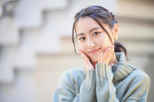 目を閉じて両手で頬を触る女性