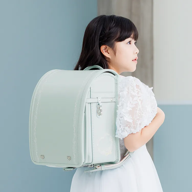 Romelia ロメリア 花々と輝くストーンの調べが 奏でるランドセル ロメリアランドセルには、愛らしいお花のモチーフ が散りばめられており、花びらの形のかぶせには、フラワーのブローチが可憐で上質な雰囲気を演出。前ポケットに描かれたお花畑のような小花柄が、ロメリア